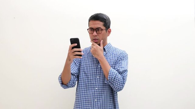 Adult Asian man showing shocked face expression after looking at his mobile phone