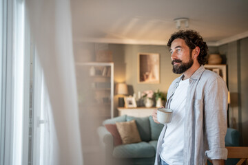 Thoughtful man drinking coffee and looking out window at home
