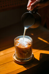 Hand Pouring Milk into Iced Coffee on Wooden Table in Natural Light