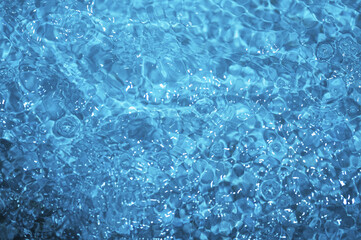 Blue water with ripples. Defocus blurred bleu clear calm water surface texture with splashes and bubbles.
