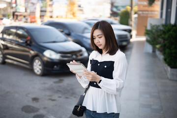 Obraz premium Young woman writing in a notebook outside on a sunny day with cars in the background in a busy urban area