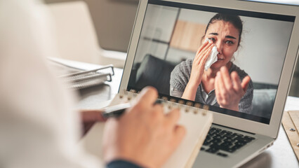 Female psychologist calms down emotional crying woman patient by video call on computer