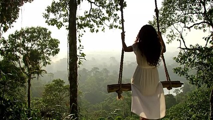 the thrill of a jungle swing in Indonesia. A solitary figure glides over a misty, green canopy during golden hour, capturing adventure and freedom. Ideal for travel and lifestyle.