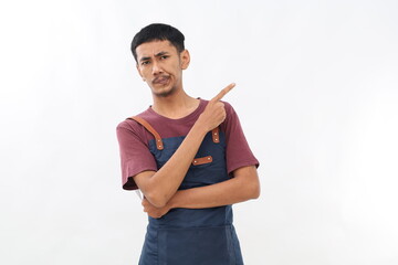 Displeased asian barista in blue apron pointing finger at upper left corner, grimacing skeptical,...