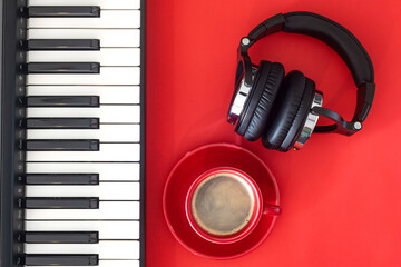 Red cappuccino coffee cup, headphones and keys of digital piano. Red background. Place for text.