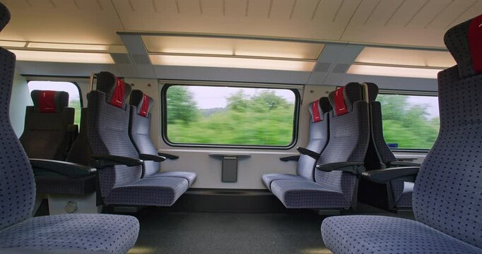 Empty first class seats inside passenger train in Europe. Large windows, moving train, blurry exterior rural  background, no people, real time, ultra wide angle view