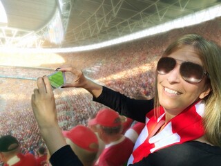 Smiling woman taking photo with a mobile phone at a football match