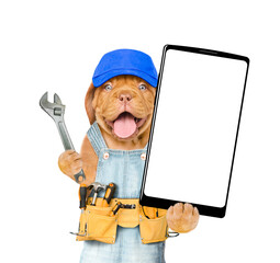 Funny Mastiff puppy wearing blue cap and denim overalls with tool belt showing big smartphone with white blank screen in it paw. Isolated on white background
