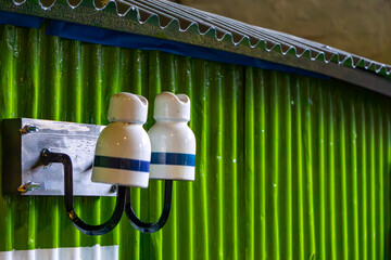 Double porcelain electrical insulator mounted on a metal bracket against a green corrugated sheet...