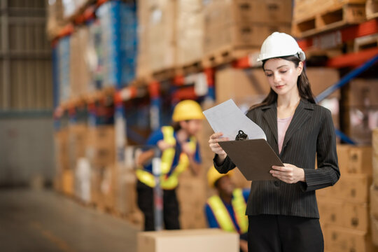 Female logistics coordinator standing in warehouse. She’s supervising goods and staff, dressed professionally for a modern work environment. Logistics and supply chain concept.