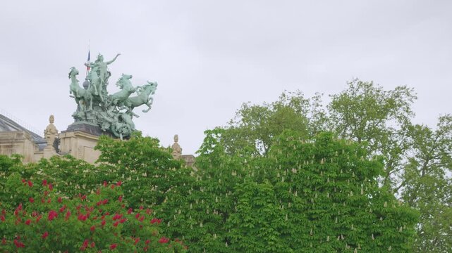 View of blossoming white and pink chestnut trees and on the one of two copper quadriga statues, also known as Recipon Quadrigas, atop the building the Grand Palais in Paris, France.