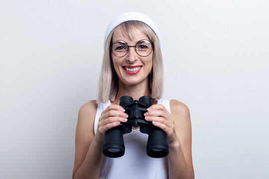Smiling young blonde woman with binoculars on a light background