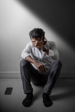 Depressed man sitting alone on the floor in dramatic lighting, covering face with hand, feeling hopeless and emotionally overwhelmed