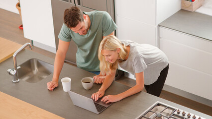 Overhead View Of Couple Looking At Laptop In Modern Kitchen