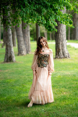A beautiful young woman with long wavy hair in a floral vintage corset and black dress posing outdoors in a lush lilac garden. Springtime atmosphere, romantic and fairytale vibes. 