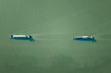 Aerial top down view of two barges navigate a river under serene conditions amid lush green waters.