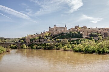 Panoramic view of Toledo with the Alcázar fortress, the Tagus River, and the historic Alcántara Bridge, blending architecture, nature, and medieval heritage