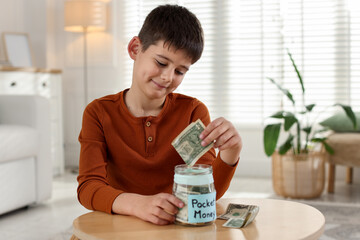 Boy putting his pocket money into jar at table indoors