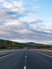 A long, open highway leads through a picturesque mountainous area.