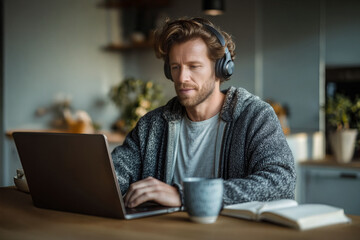 Caucasian man working from home with laptop and headphones in cozy setting