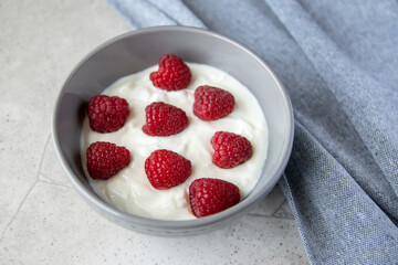 Gray bowl and natural yogurt with red berries on the stone marble table.