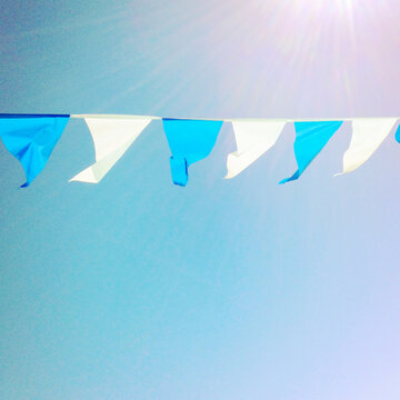 Row of blue and white bunting hanging in front of a blue sky