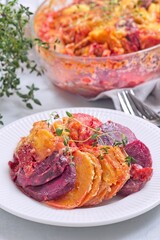 Sweet potato, parsnips and beet root au gratin with thyme and melted cheese, on plate, vertical