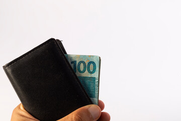 a man's hand holding a wallet with Brazilian 100 reais notes