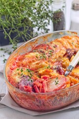 Sweet potato, parsnips and beet root au gratin with thyme and melted cheese, in glass dish, vertical