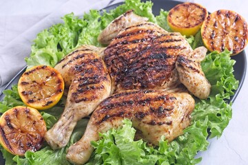 Grilled spatchcocked chicken with lemon garlic marinade on lettuce with lemon halves, horizontal