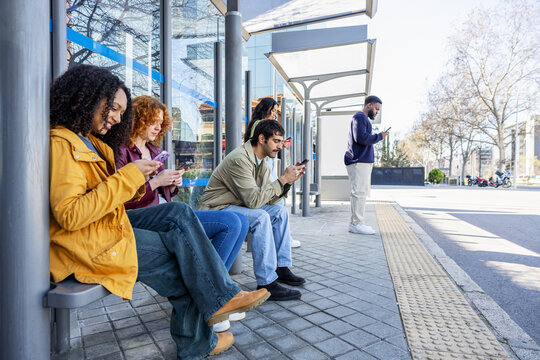 Diverse group of young adults immersed in their phones at a city bus stop