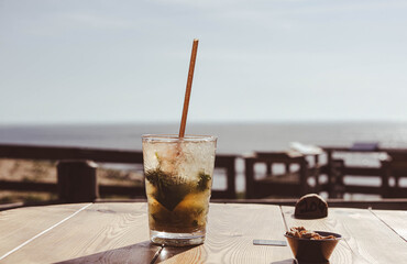 Chilled mojito served with a straw with the ocean in the background.
