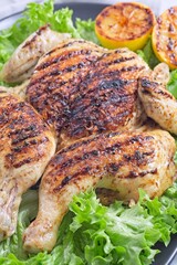 Grilled spatchcocked chicken with lemon garlic marinade, with lettuce and lemon, vertical closeup