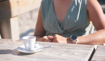 Beautiful young woman enjoying an espresso served on a terrace with the ocean in the background.