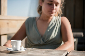 Beautiful young woman enjoying an espresso served on a terrace with the ocean in the background.