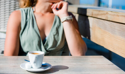 Beautiful young woman enjoying an espresso served on a terrace with the ocean in the background.