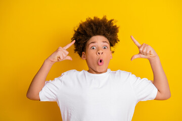 Playful young boy making expressive gestures against bright yellow background wearing a white t-shirt