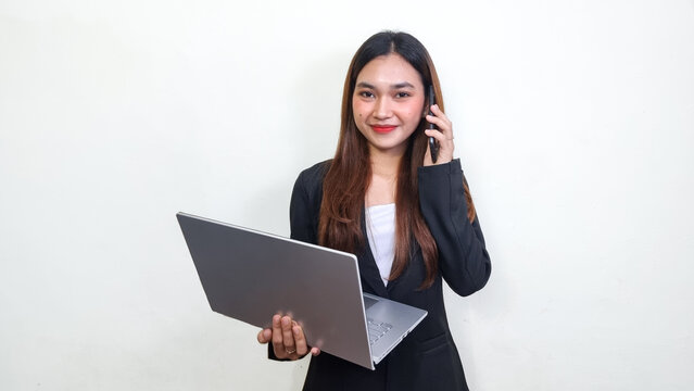 Beautiful and successful asian business woman. Office woman in black suit holding laptop smiling at camera while receiving call from smartphone. Knowledgeforall. 