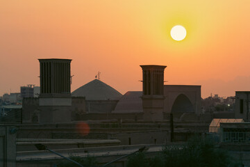 Scenic sunset over the historic skyline of Yazd, Iran, featuring traditional windcatchers and domes bathed in golden light.