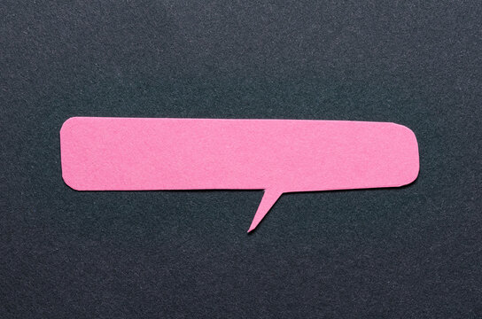 Pink cut out blank paper speech bubble of rectangular shape and rounded corners with copy space for text on dark background, flat lay top view conceptual backdrop