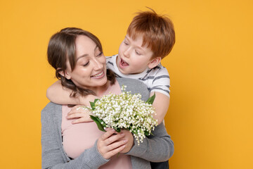 Boy giving his mother beautiful bouquet of lily-of-the-valley flowers on yellow background