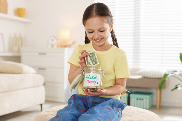 Girl putting her pocket money into jar at home