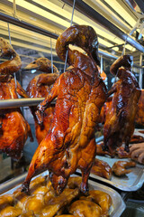 Close-up of glistening roast ducks hanging in a row at a hawker-style food stall. The ducks are...