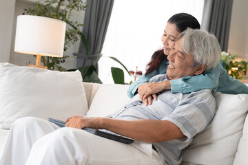 Obraz premium Asian senior woman embracing husband on couch afther finish working with laptop. Family love and support concept. Couple spending time together at home