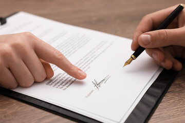 Woman pointing at document and man putting signature at wooden table, closeup
