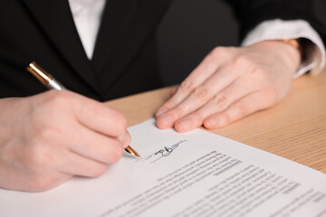 Woman putting signature on document at wooden table, closeup