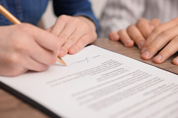 Woman putting signature on document at table, closeup