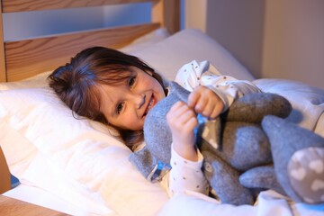 Smiling little girl with toy in bed at home