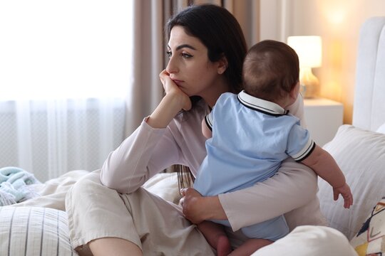 Woman suffering from postpartum depression with her little baby on bed at home