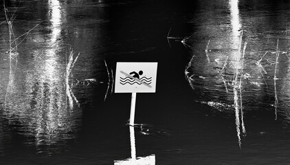 Flooded area with swimming warning sign partially submerged in water reflecting surrounding...